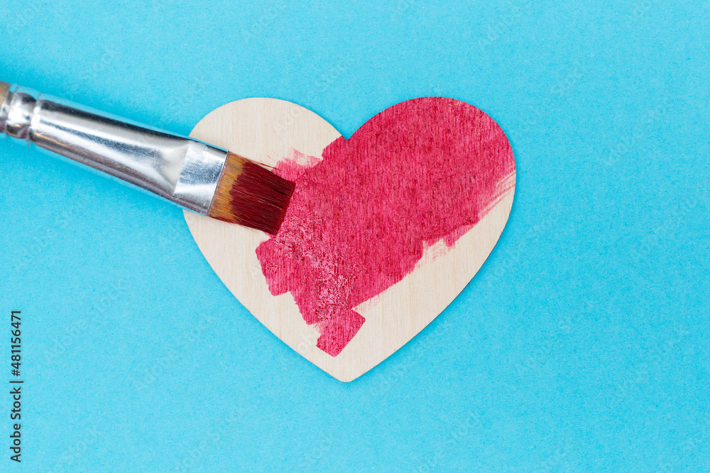 Wall mural Man paints a wooden heart with red paint. Blue background. Flat lay. Love concept. Handmade heart. Flat lay. Valentine Day