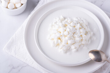 Fresh cottage cheese grain in a white bowl and marshmallows. Curd in granules with cream. Copy space