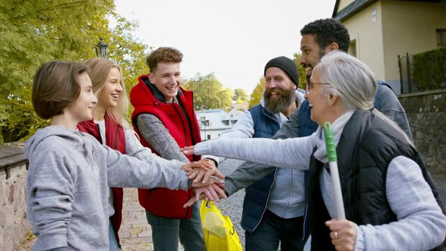 Diverse group of happy community service volunteers stacking hands together outdoors in street