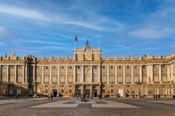 Madrid, Spain - November 30, 2021: Front view of the facade of the Royal Palace of Madrid from Plaza de la Armeria Square. Real people-tourists against the backdrop of a beautiful old Spanish castle