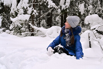 Fototapeta na wymiar cheerful pretty girl is sitting on her knees in snowdrift and laughing. Outdoor activities in winter forest.