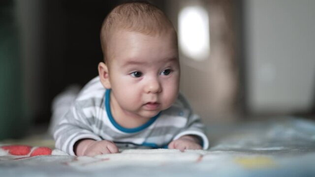 Baby boy in striped shirt struggling to hold his head up. Lovely kid with plump cheeks close up. Blurred backdrop.