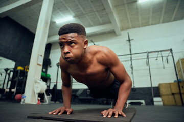 Fototapeta na wymiar Young African American male doing push-ups in the gym. Mixed race, male personal trainer doing cross fit indoors. High quality photo