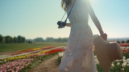 Young woman with camera and straw hat turning around in beautiful tulips garden.