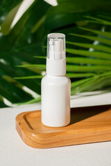 Plastic white tube for lotion with pomp on wooden plate against the background of palm leaves. Skin...