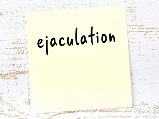 Yellow sticky note on wooden wall with handwritten word ejaculation