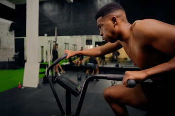 Fototapeta na wymiar African American male using an elliptical trainer during cross training. Male athlete exercising intensely in the gym. High quality photo