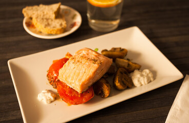 steamed sea trout fillet served on fried mushrooms with tomatoes on a white plate