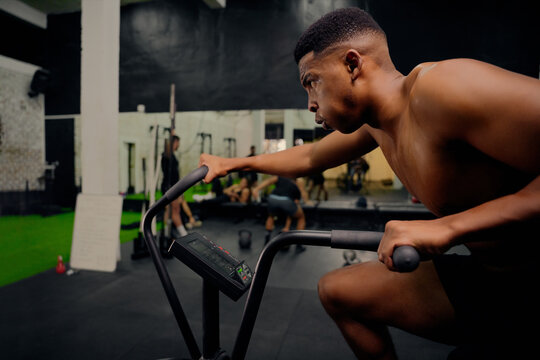 African American male using an elliptical trainer during cross training. Male athlete exercising intensely in the gym. High quality photo