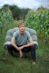 Child boy sitting on a armchair in a field in the countryside.