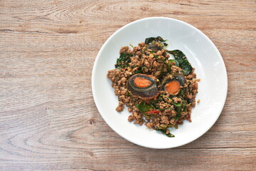 slice boiled  black preserved egg dressing spicy fried chop pork and basil leaf on plate