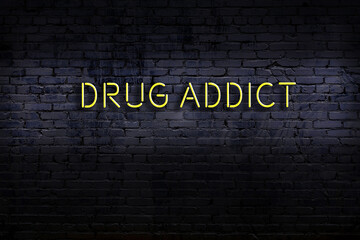 Neon sign. Word drug addict against brick wall. Night view