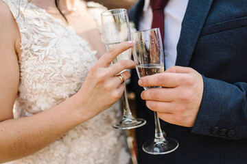 Newlyweds holding glasses of champagne for toast in hands of the outdoor. Standing on wedding...