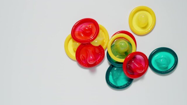 SLOW: Many colour condoms fall on a white table - Close Up, Top view