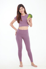 Beautiful Asian woman with good figure wearing purple workout clothes holding broccoli standing on a white background. fitness concept Weight loss, choosing healthy, clean, chemical-free food