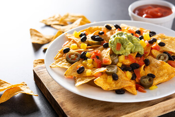 Mexican nachos tortilla chips with black beans, guacamole, tomato and jalapeno on black background. Copy space