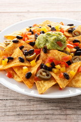 Mexican nachos tortilla chips with black beans, guacamole, tomato and jalapeno on wooden table. Close up