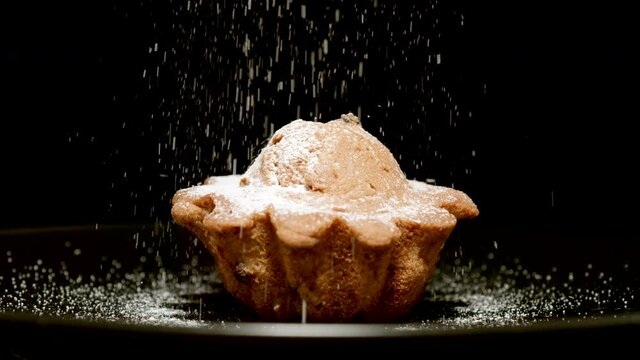 Powdered sugar falls on a fresh cupcake on a black background