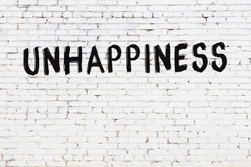 White wall with black paint inscription unhappiness on it