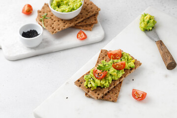 Sandwich with avocado paste on bread with tomatoes cherry and arugula on white table.