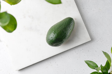 Green avocado on a white marble board with green leaves. Top view, food composition