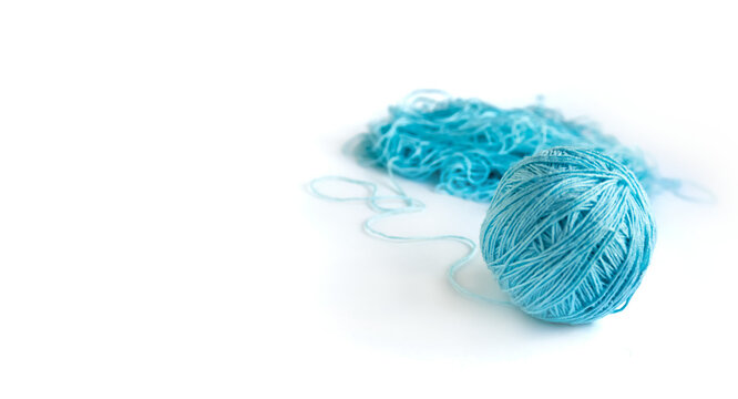 A ball of blue fine cotton yarn in the process of winding on the white background. Tangled yarn in the background. Banner with space for text on the left