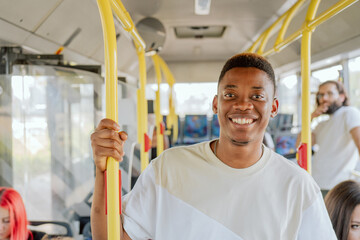 A dark-skinned man stands in the middle of a bus going home, work, he is smiling, looking into the...