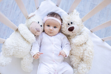 baby girl with teddy bears smiling on the bed on a white cotton bed, falling asleep or waking up in the morning, cute newborn little baby at home in the crib close-up