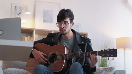 Guitar video course. Music education. Creative occupation. Inspired talented guitarist beginner guy practicing playing instrument using laptop at modern home interior.