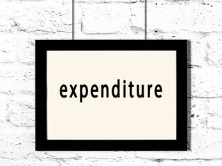 Black frame hanging on white brick wall with inscription expenditure