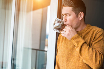 Fototapeta na wymiar Man in knitted wool sweater drinks tea a cup, relax at home in autumn day. Health care, authenticity, sense of balance and calmness. Fresh air.