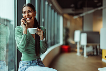 Smiling caucasian consultant, taking a sip of her coffee, talking on her phone.