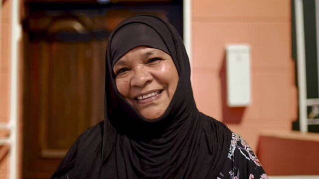 Happy muslim woman smiling at the camera while standing outside her home. Mature modest woman wearing a black hijab.