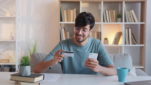 Internet payment. Mobile banking. Digital money transaction. Relaxed satisfied guy using credit card smartphone app at modern home workplace interior.