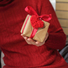 gift in a hand decorated with a heart symbol knitted from threads by hand close-up. warm tender feelings
