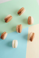 Chocolate and coffee french macarons cookies on colorful pastel background, top view.