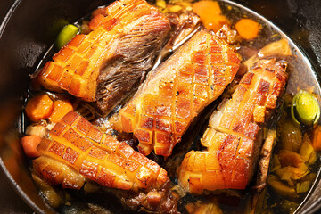 Golden brown crispy pork shoulders prepared with vegetables and seasoning in roast pot on kitchen...