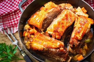 Golden brown crispy pork shoulders prepared with vegetables and seasoning in roast pot on kitchen table
