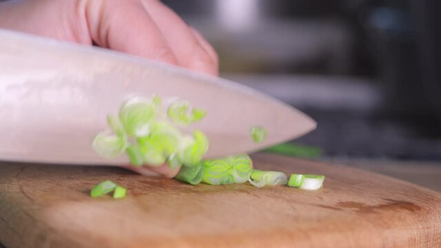 a woman's hand cuts green onions with a knife on a wooden chopping board. Slicing greens for salad