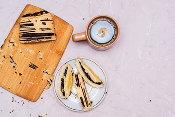 sliced puff pastry bun with poppy seeds and chocolate on a cutting board and on a saucer and a coffee mug top view copy space