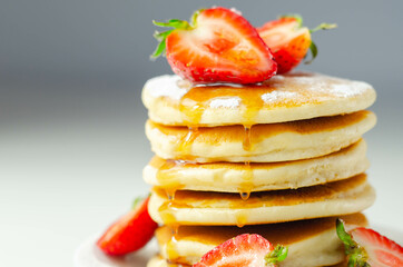 Delicious pancakes stacked with fresh sweet strawberries, topped with maple syrup