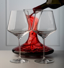 Glasses for wine, against the background of a decanter into which red wine is poured from a bottle, on a light background