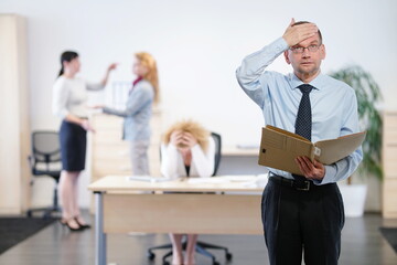 3 Büroangestellte streiten im Hintergrund, während der Chef schockiert von der Situation ist