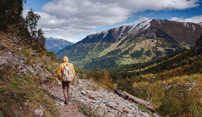 Fototapeta na wymiar travel to Caucasus mountains in Karachay-Cherkessia, Arkhyz. Man in yellow hipster hoodie hiking in mountains with travel backpack. Wandering lifestyle, adventure concept autumn vacation in wild