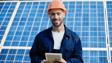 happy engineer in hardhat holding gadget near solar panel
