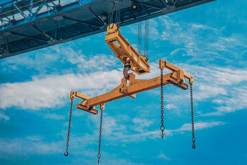 The crane moves a reinforced metal product with hooks. Yellow crane beam on a blue sky background.