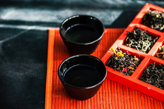 Two cups of green tea next to a box of assorted loose leaf teas on a table