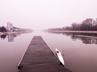 Naklejka premium View to a lake, pier, boat and misty sky