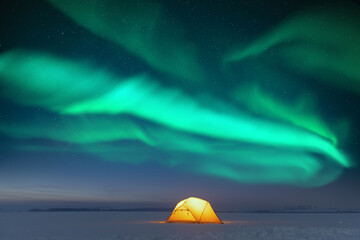 Yellow tent lighted from the inside against the backdrop of incredible starry sky with Aurora borealis. Amazing night landscape. Northern lights in winter field © Ivan Kmit