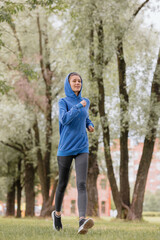 Obraz premium a European woman in a blue hoodie is running and doing sports in the park. fitness and yoga outdoor sports, exercise and meditation and fitness for body health. spiritual development. outdoor sports